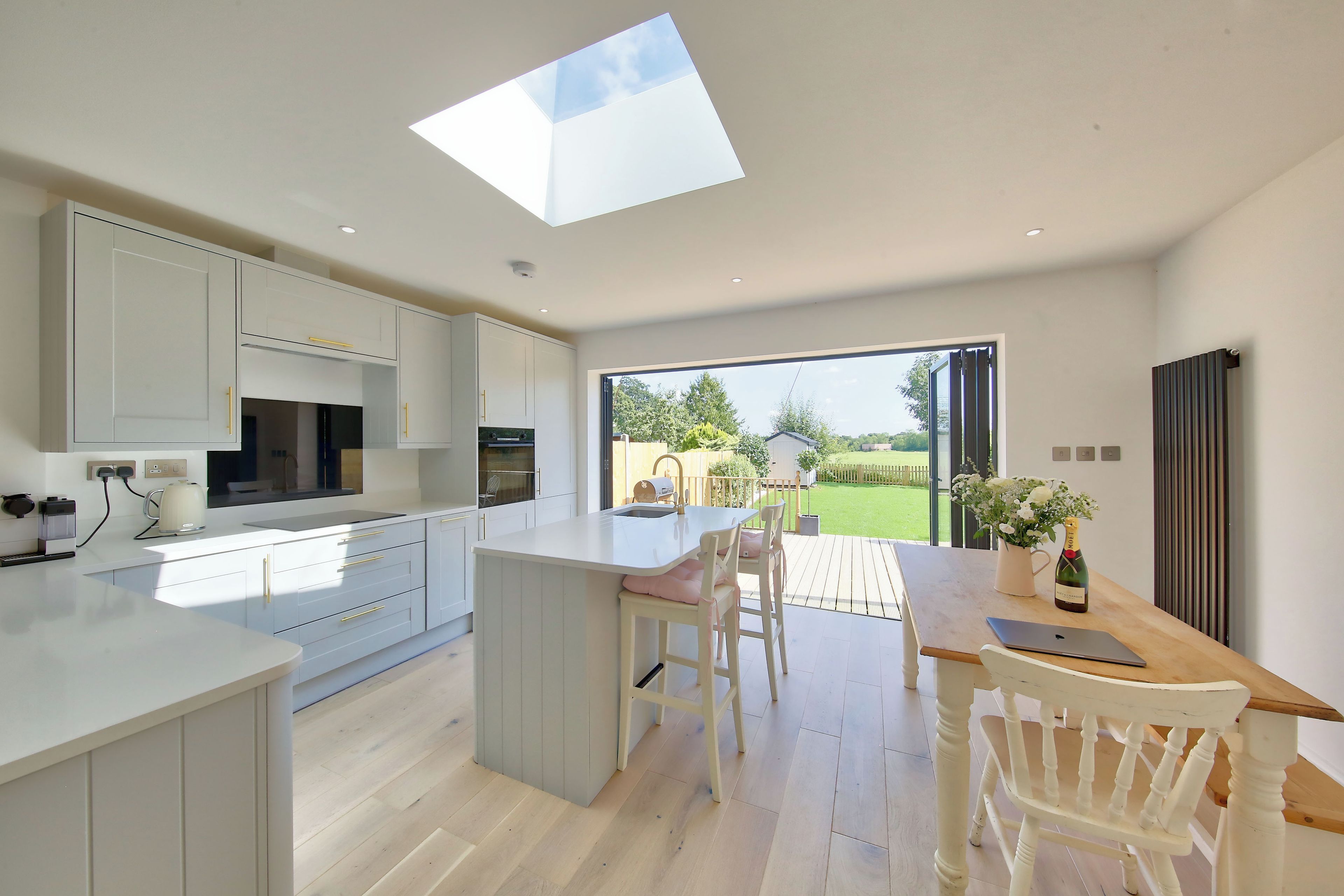 A modern kitchen with a large island, a dining area with a table and chairs, and a view of a garden through an open door.