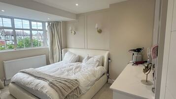 A bedroom with a large bed, a bedside table with a lamp, a radiator, and a window with curtains.