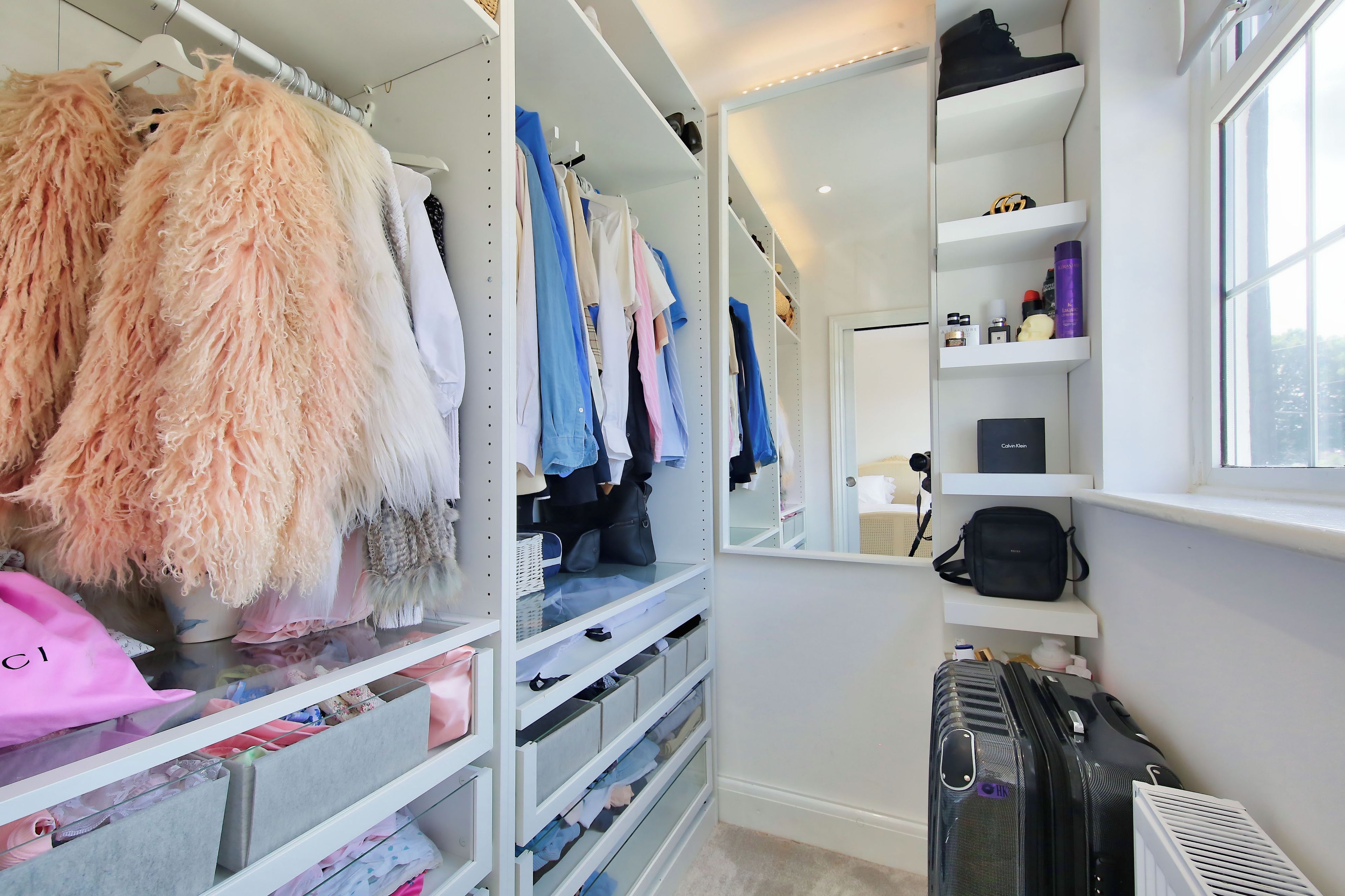 A well-organized closet with hanging clothes, shelves with various items, and a suitcase.