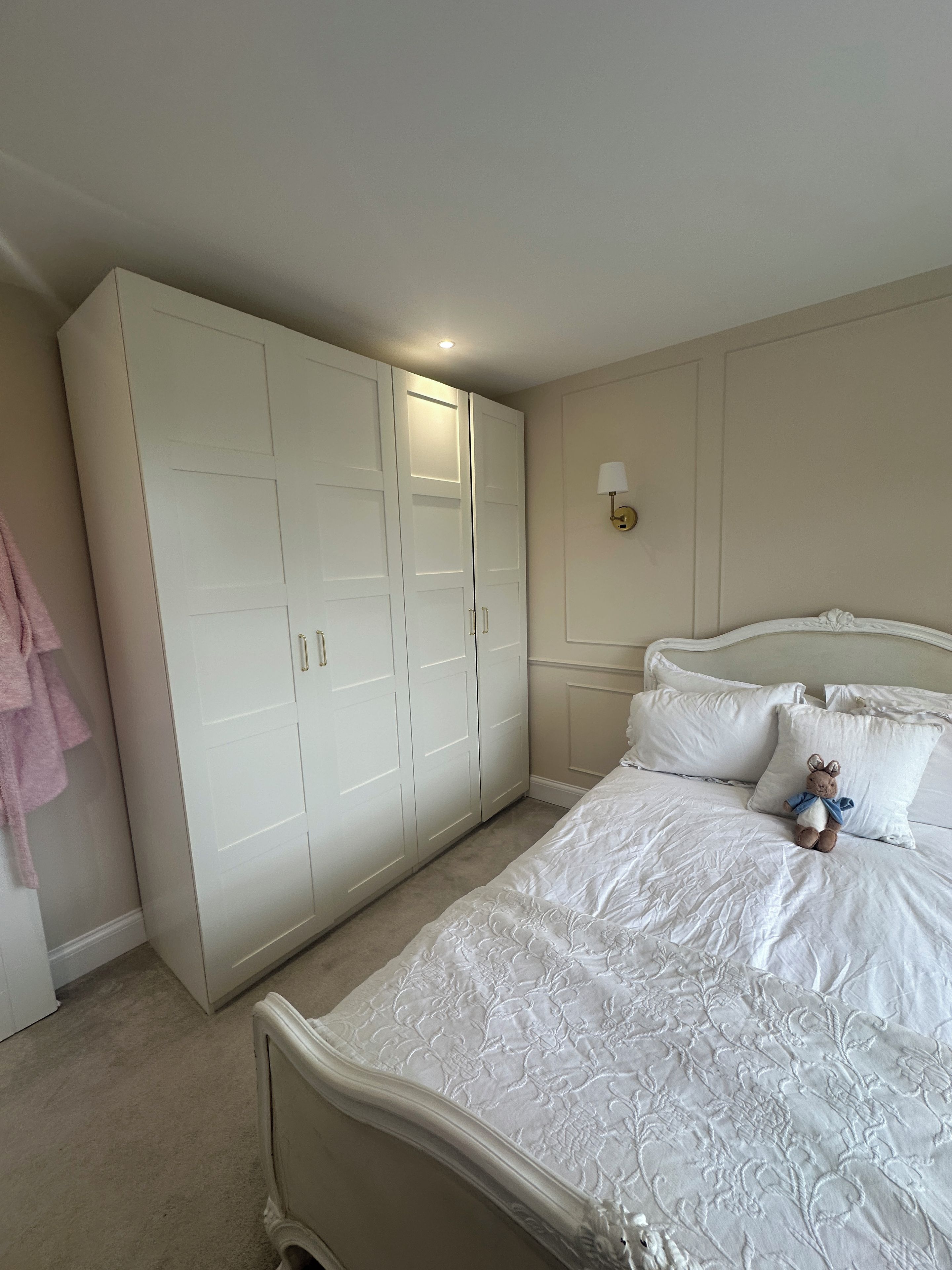 A bedroom with a large wardrobe, a bed with white bedding, and a wall-mounted lamp.