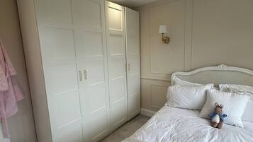 A bedroom with a large wardrobe, a bed with white bedding, and a wall-mounted lamp.