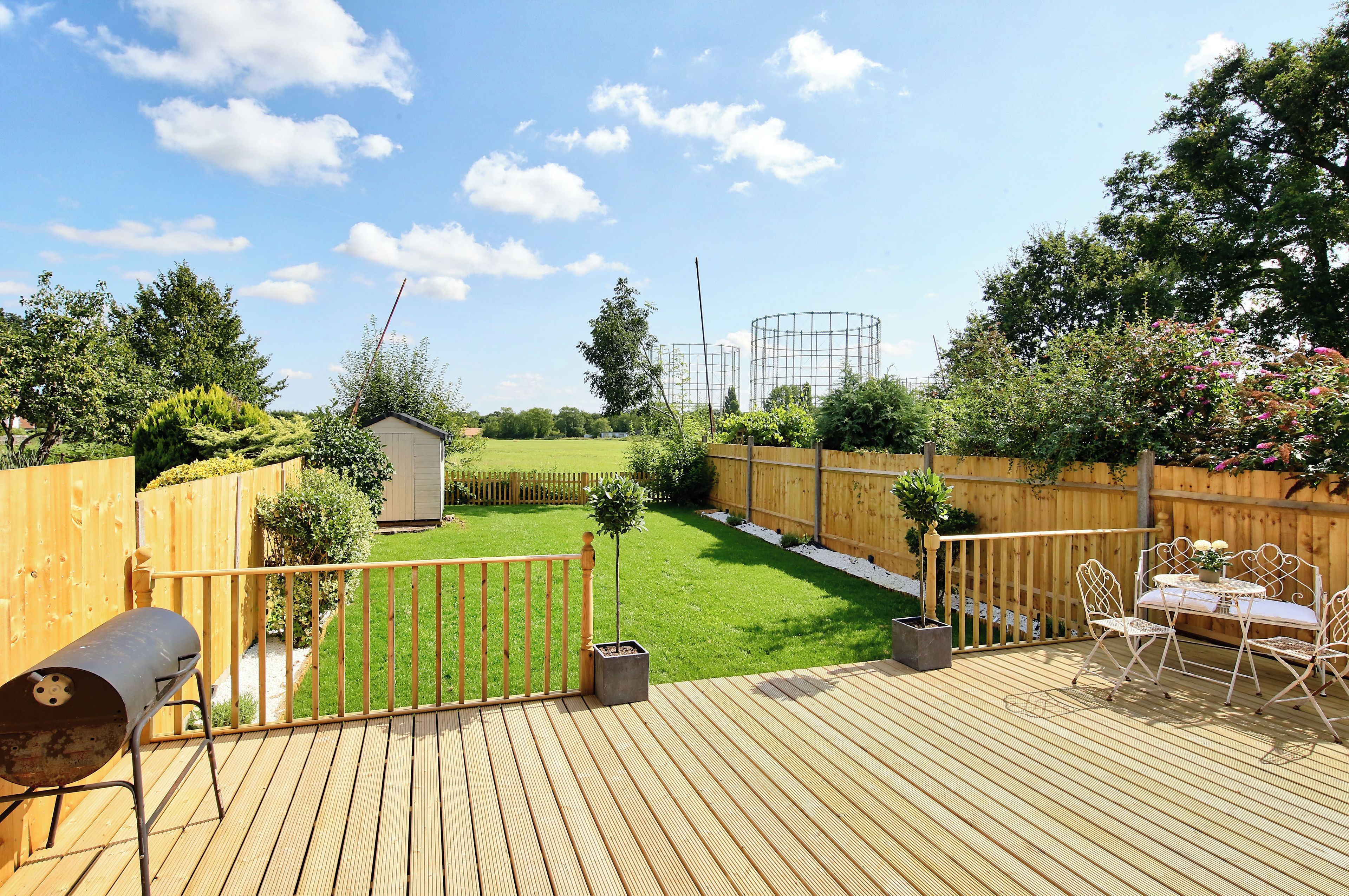 A wooden deck with a barbecue grill, a small shed, and a fenced garden area with a lawn and trees.