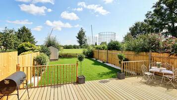 A wooden deck with a barbecue grill, a small shed, and a fenced garden area with a lawn and trees.