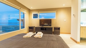 A hotel room with a large bed, a TV, a desk, and a view of the sea.