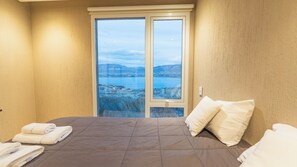 Un dormitorio con cama, almohadas y vistas a un cuerpo de agua y paisaje a través de un ventanal.