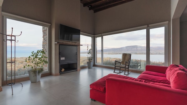 A spacious living room with a red sofa, a fireplace, and a large window offering a view of a lake and mountains.