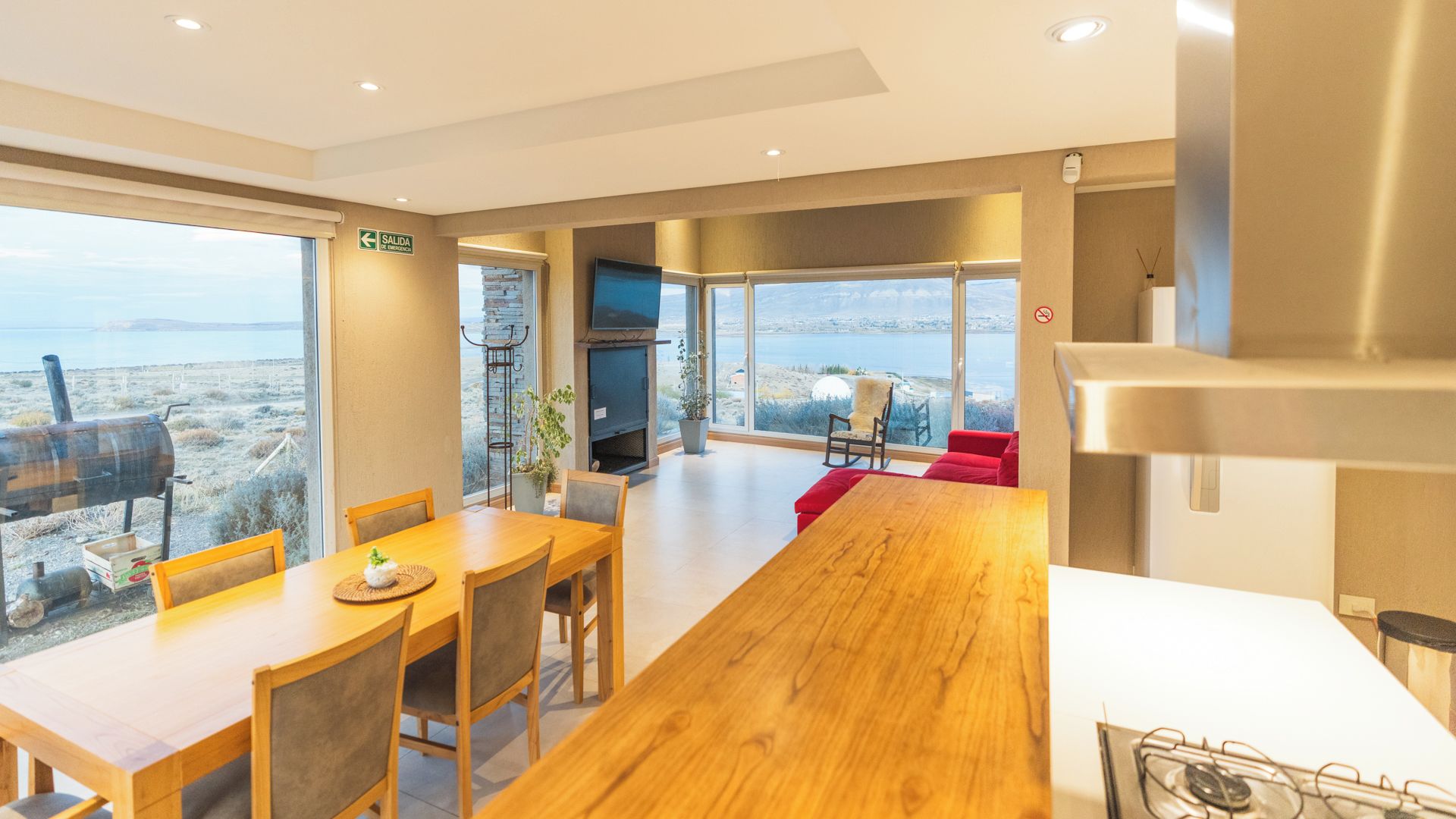 Ein modernes Interieur mit einem Holzesstisch, Stühlen, einem roten Sofa und einem großen Fenster mit Blick aufs Meer.