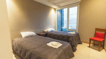 Habitación de hotel con dos camas, una ventana con vistas y una silla de madera.