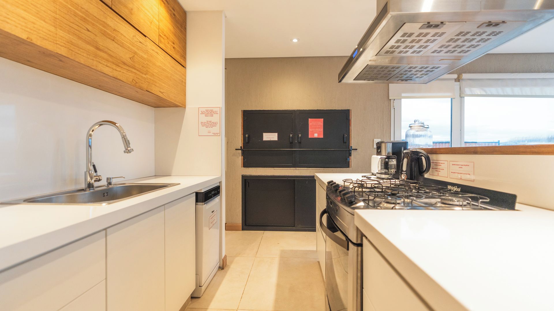 A modern kitchen with a stainless steel sink, a built-in dishwasher, a compact refrigerator, and a gas stove.