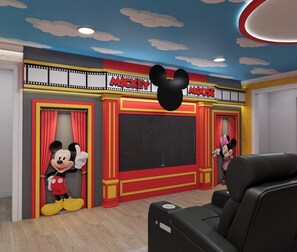 Ein Kinoraum mit einer großen Leinwand, roten Vorhängen und Aussparungen von Mickey Mouse und Minnie Mouse.