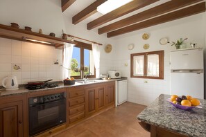 A kitchen with wooden cabinets, a stove, a microwave, and a refrigerator. - Holiday Home "Assumpcio" with Mountain View, Pool, Garden & Wi-Fi (Illes Balears)