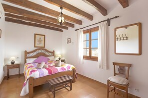 A bedroom with a wooden bed, a bench, a window with curtains, a mirror, and two bedside lamps. - Holiday Home "Assumpcio" with Mountain View, Pool, Garden & Wi-Fi (Illes Balears)