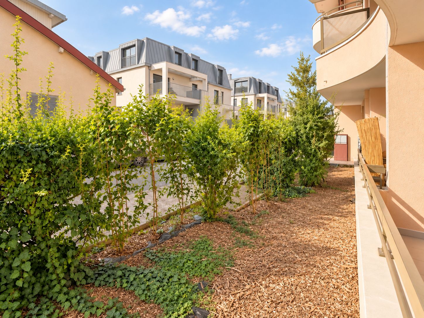 Un quartier résidentiel avec des immeubles modernes, un jardin agrémenté d’arbustes verdoyants et un sentier.