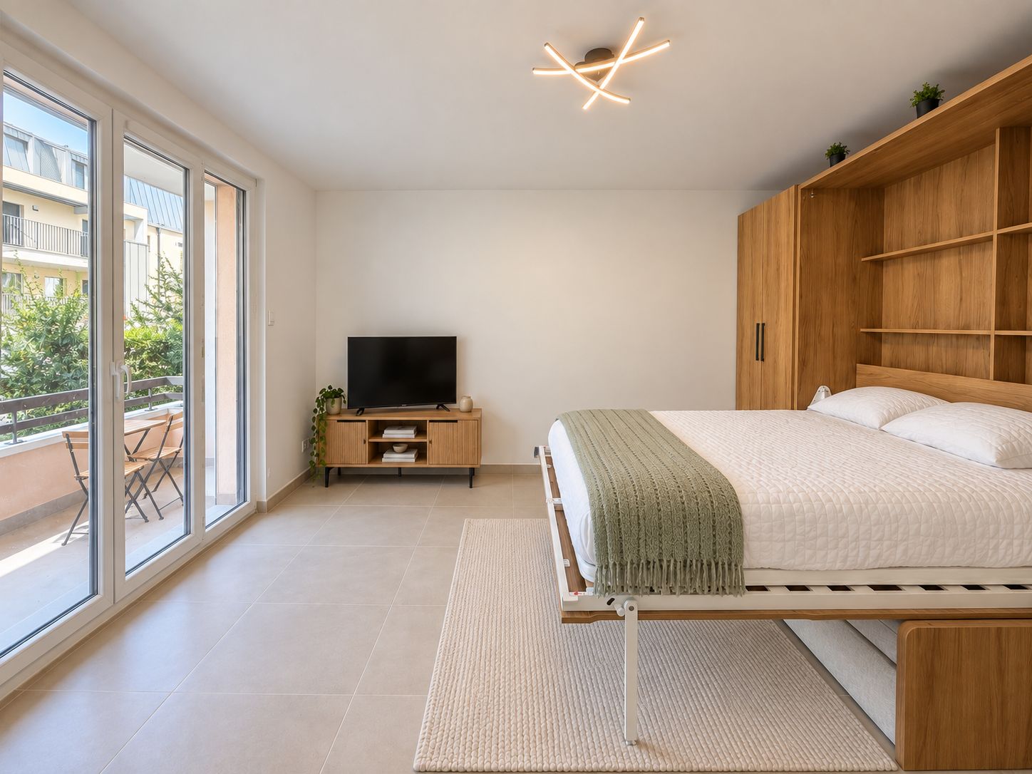 Een moderne slaapkamer met een bed, een televisie op een houten dressoir, een balkon met uitzicht en een plafondlamp.