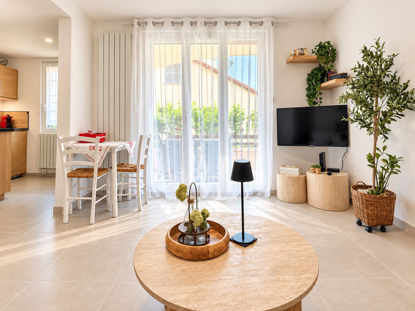 Un salon moderne avec une table ronde en bois, un téléviseur et une grande fenêtre avec des rideaux.