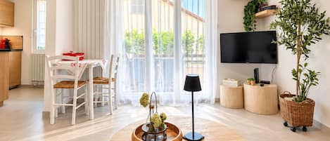 A modern living room with a round wooden table, a TV, and a large window with curtains.