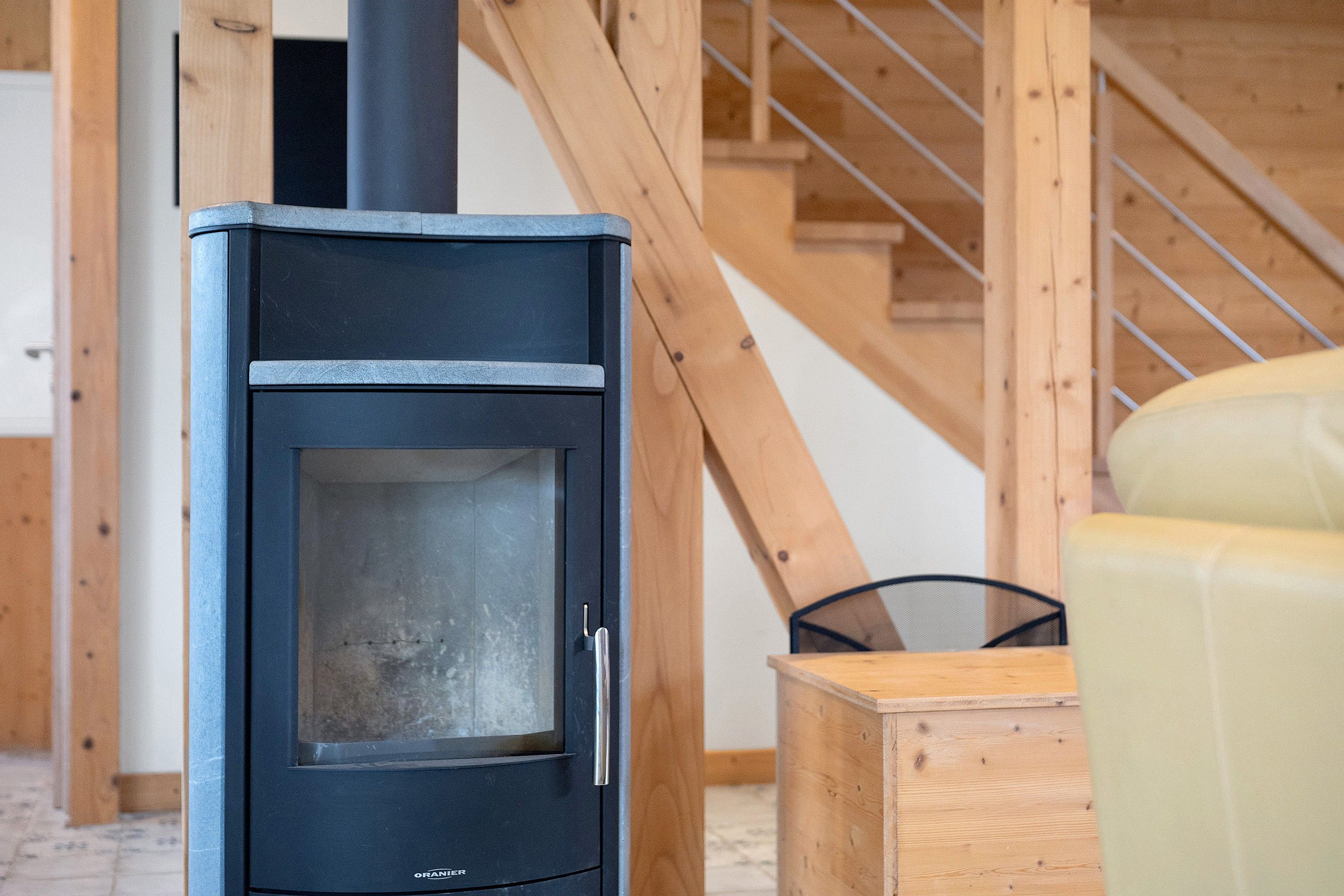A black wood-burning stove with a glass door, situated in a room with wooden beams and a metal chair.