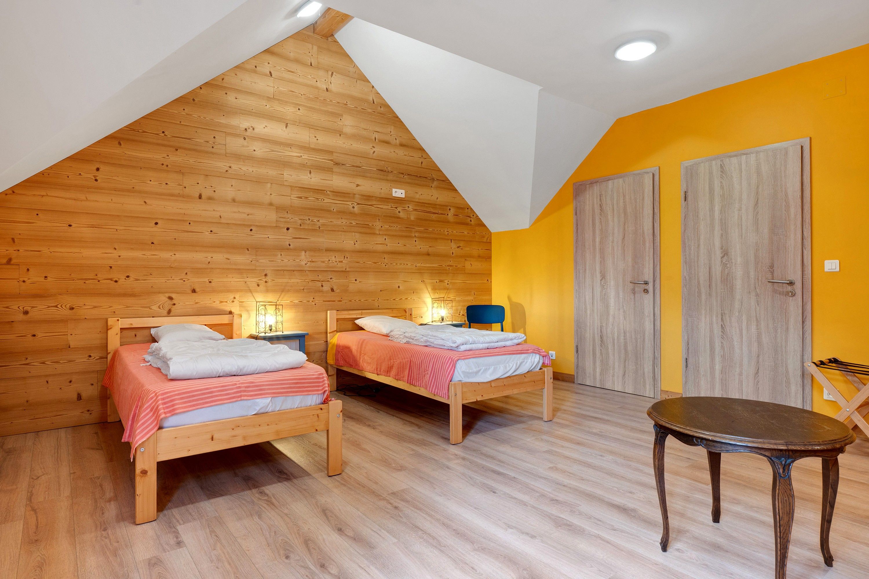 A room with two wooden beds, a small table, and a yellow accent wall.