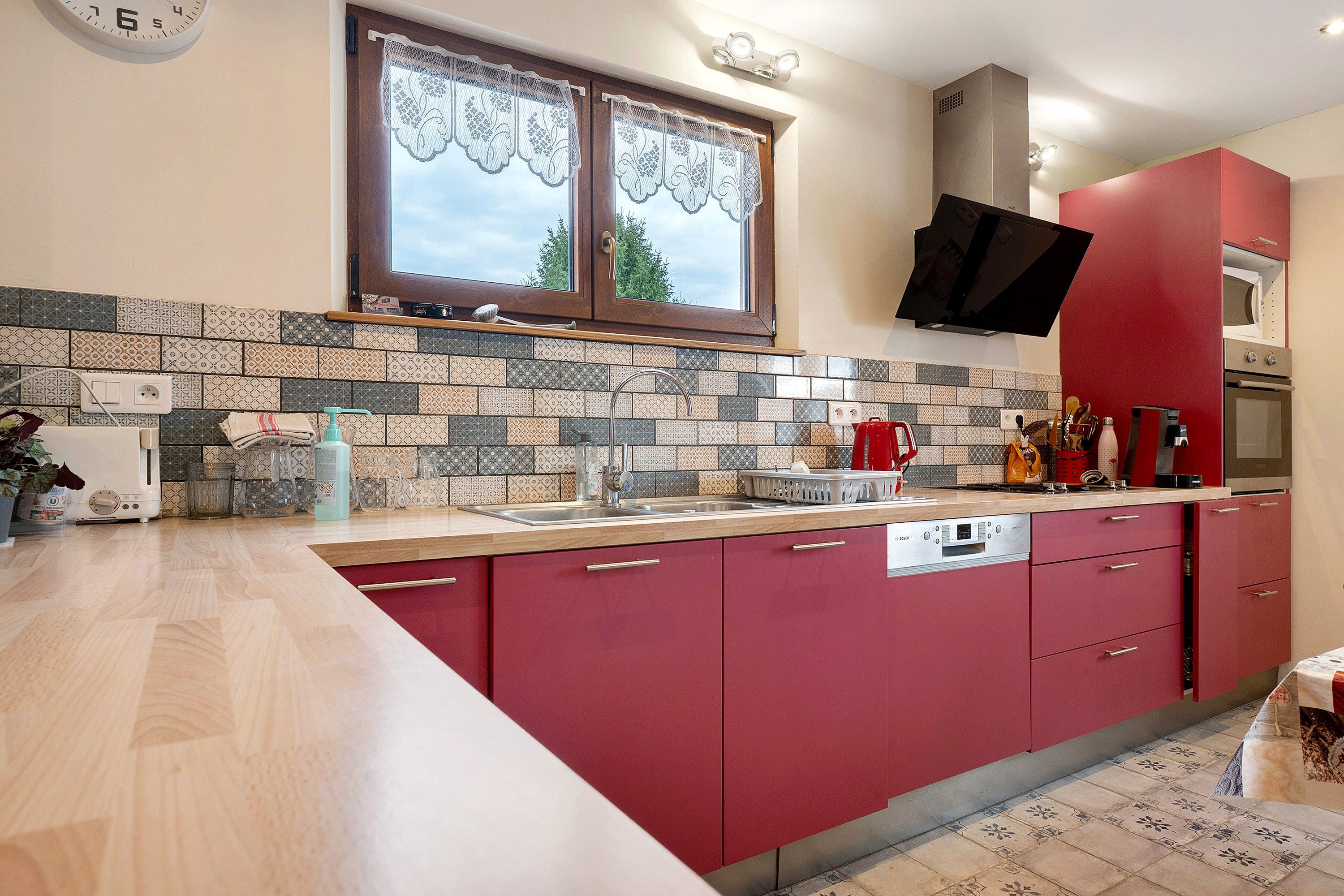 Une cuisine avec un dosseret carrelé, un lave-vaisselle encastré et un meuble de rangement rouge.