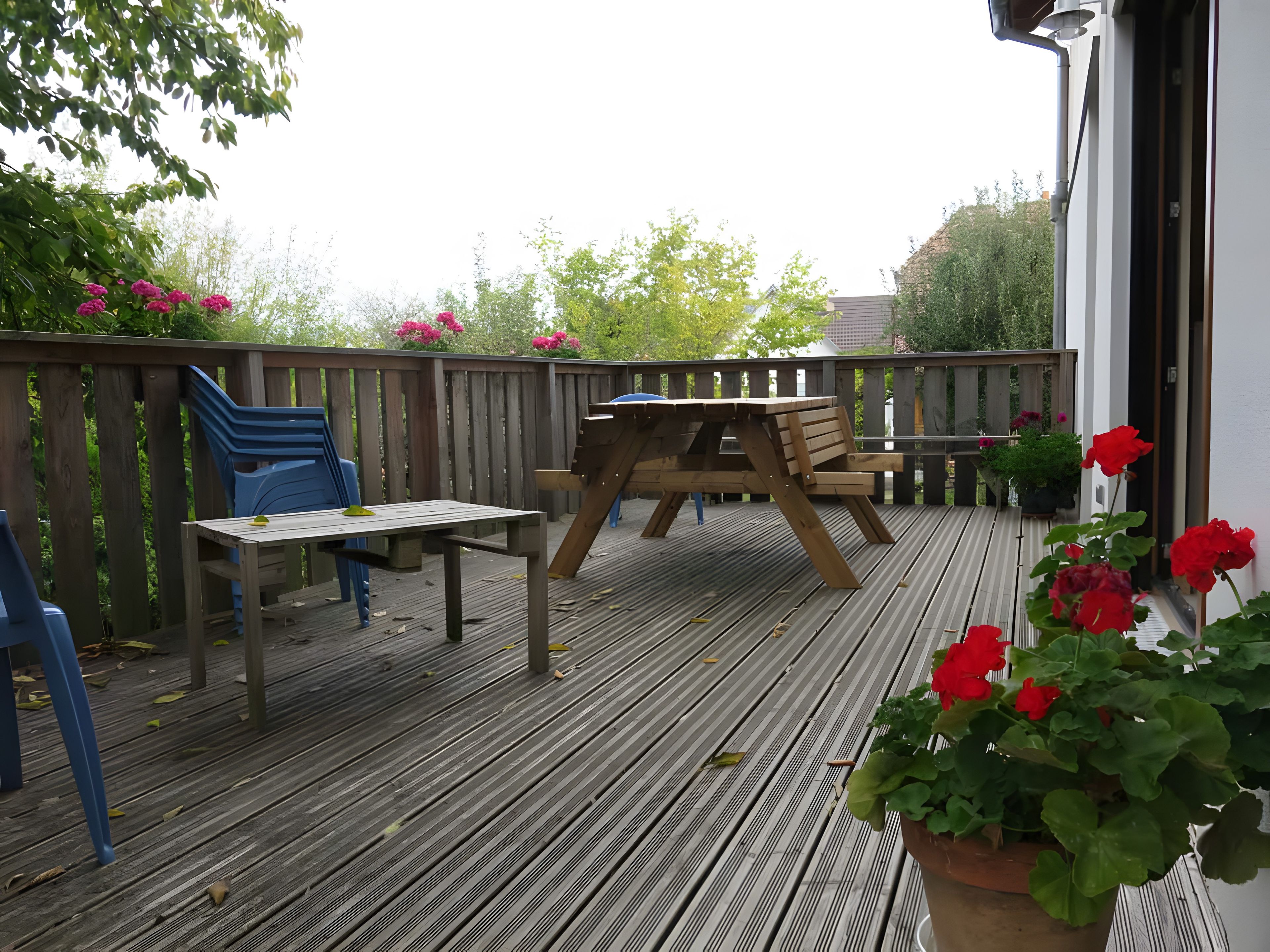 Une terrasse en bois avec une table de pique-nique et des chaises, entourée d’une clôture en bois et de plantes en pot.