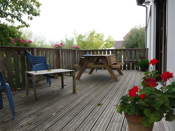 Eine Holzterrasse mit Picknicktisch und Stühlen, umgeben von einem Holzzaun und Blumentöpfen.