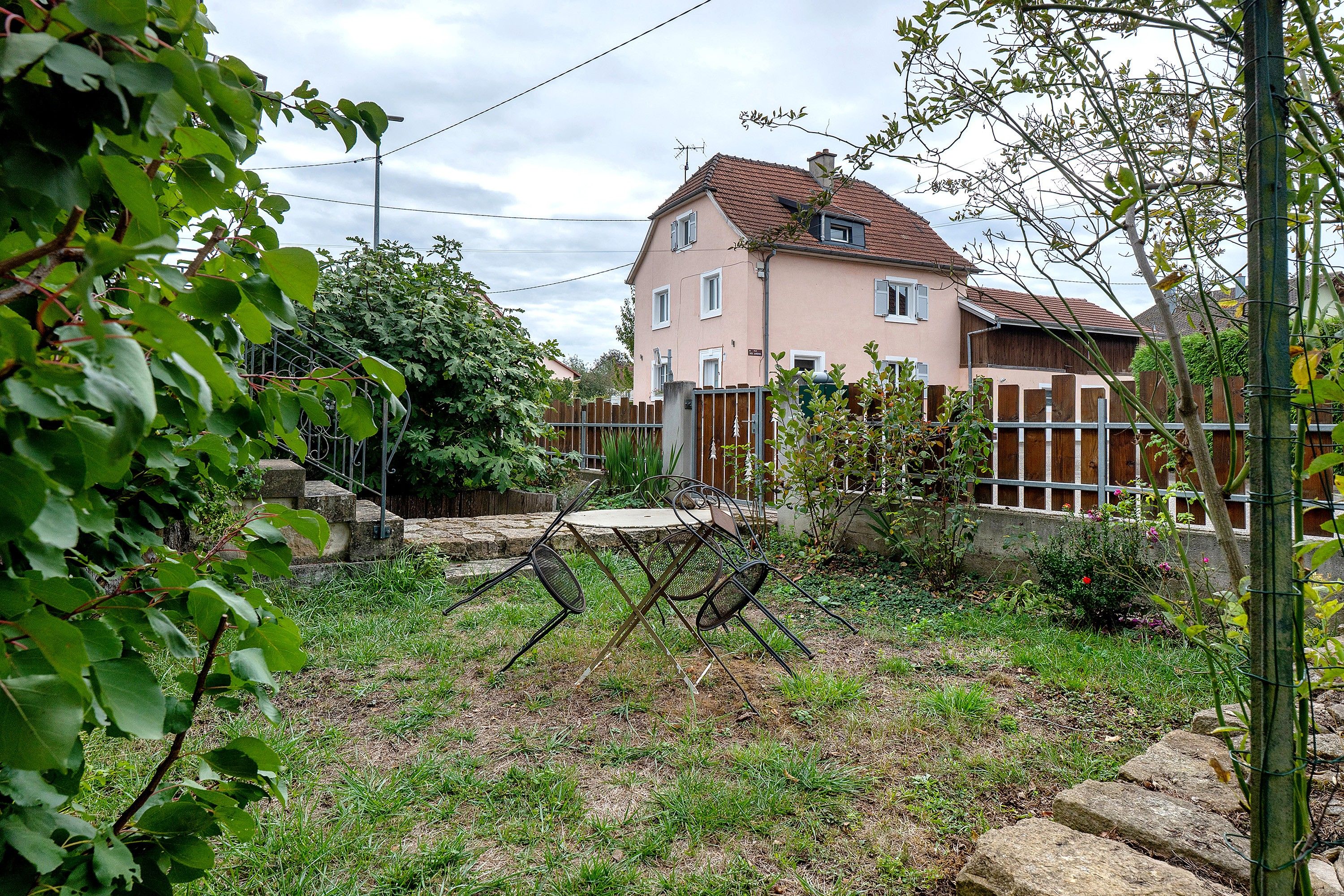 Ein Wohngebiet mit einem zweigeschossigen Haus, einem Metallzaun und einem Garten mit Rasen und Pflanzen.