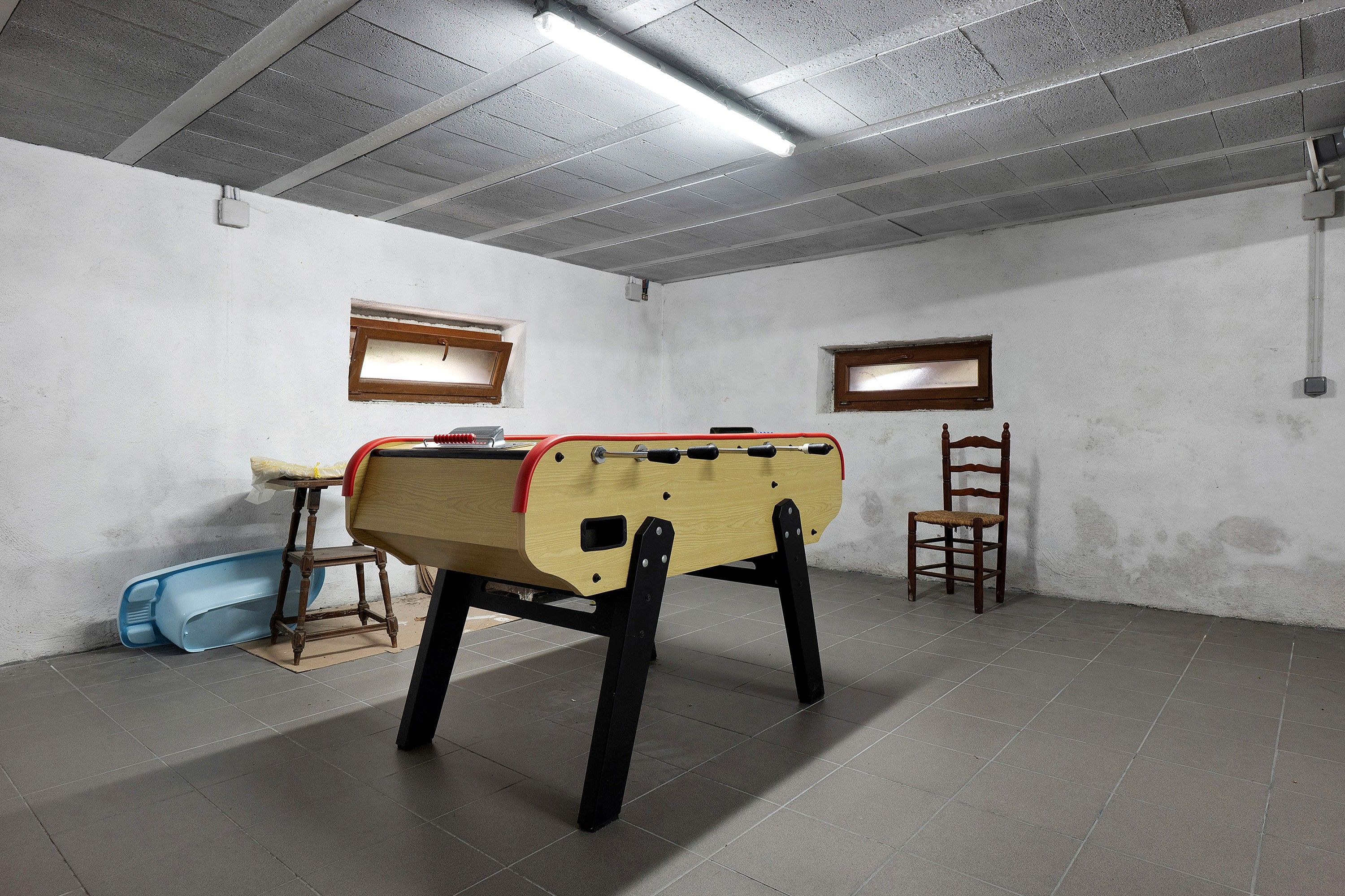 A room with a foosball table, a chair, and a small table with a blue object.