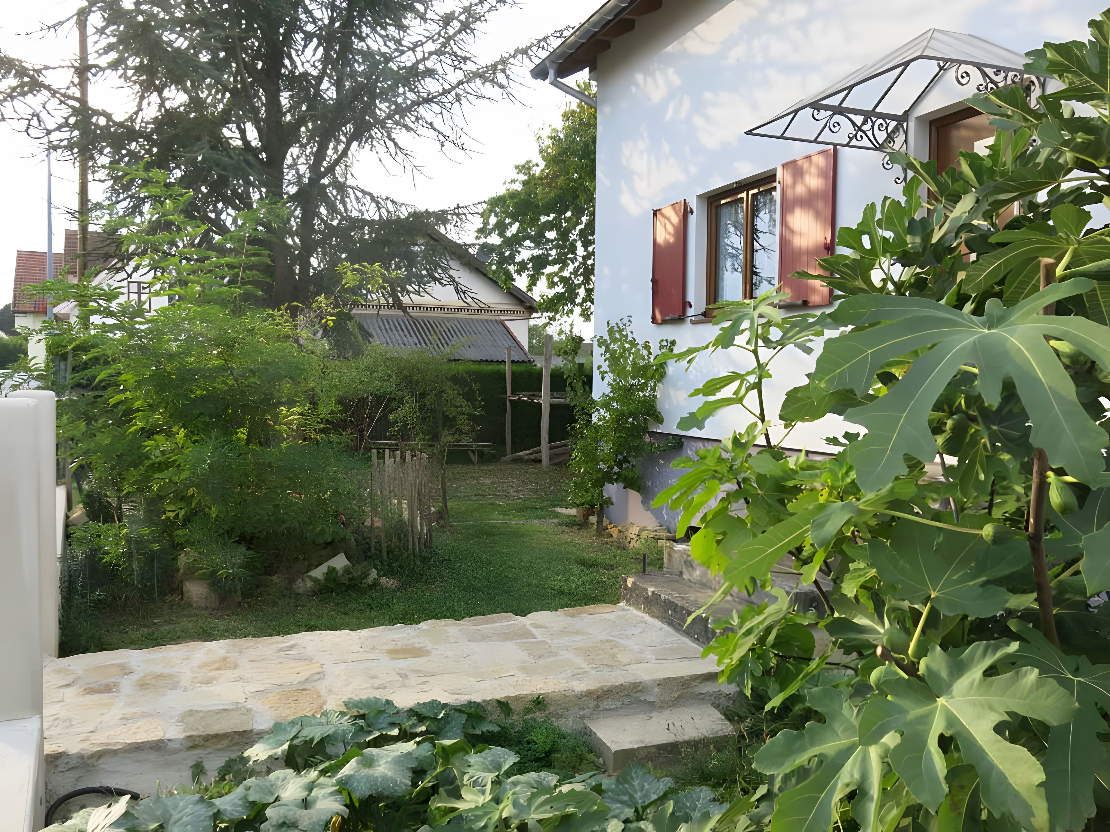 A residential property with a stone staircase leading to a wooden deck, surrounded by lush greenery and a white house with red shutters.