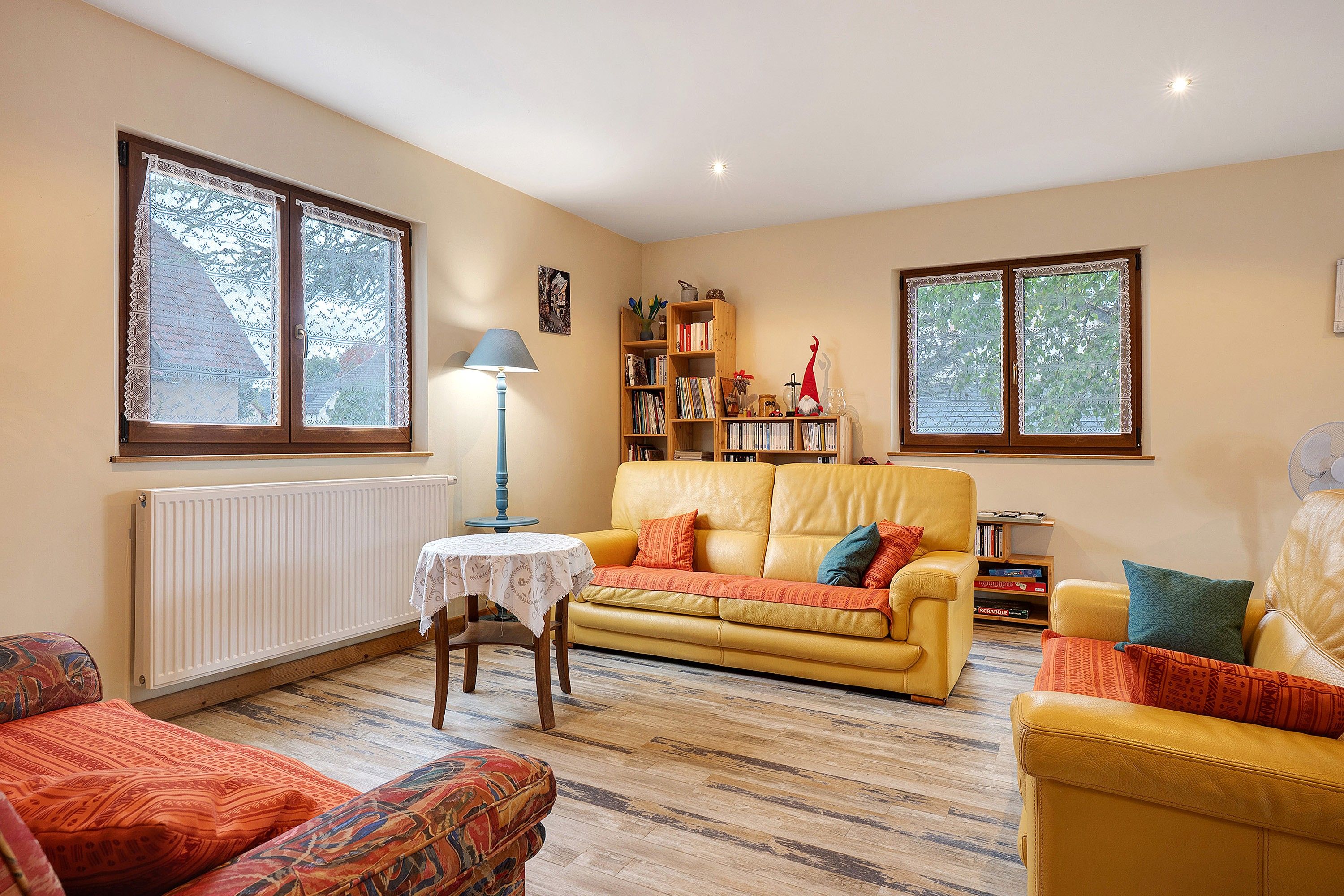 A cozy living room with a yellow sofa, a patterned armchair, and a small table with a lamp.