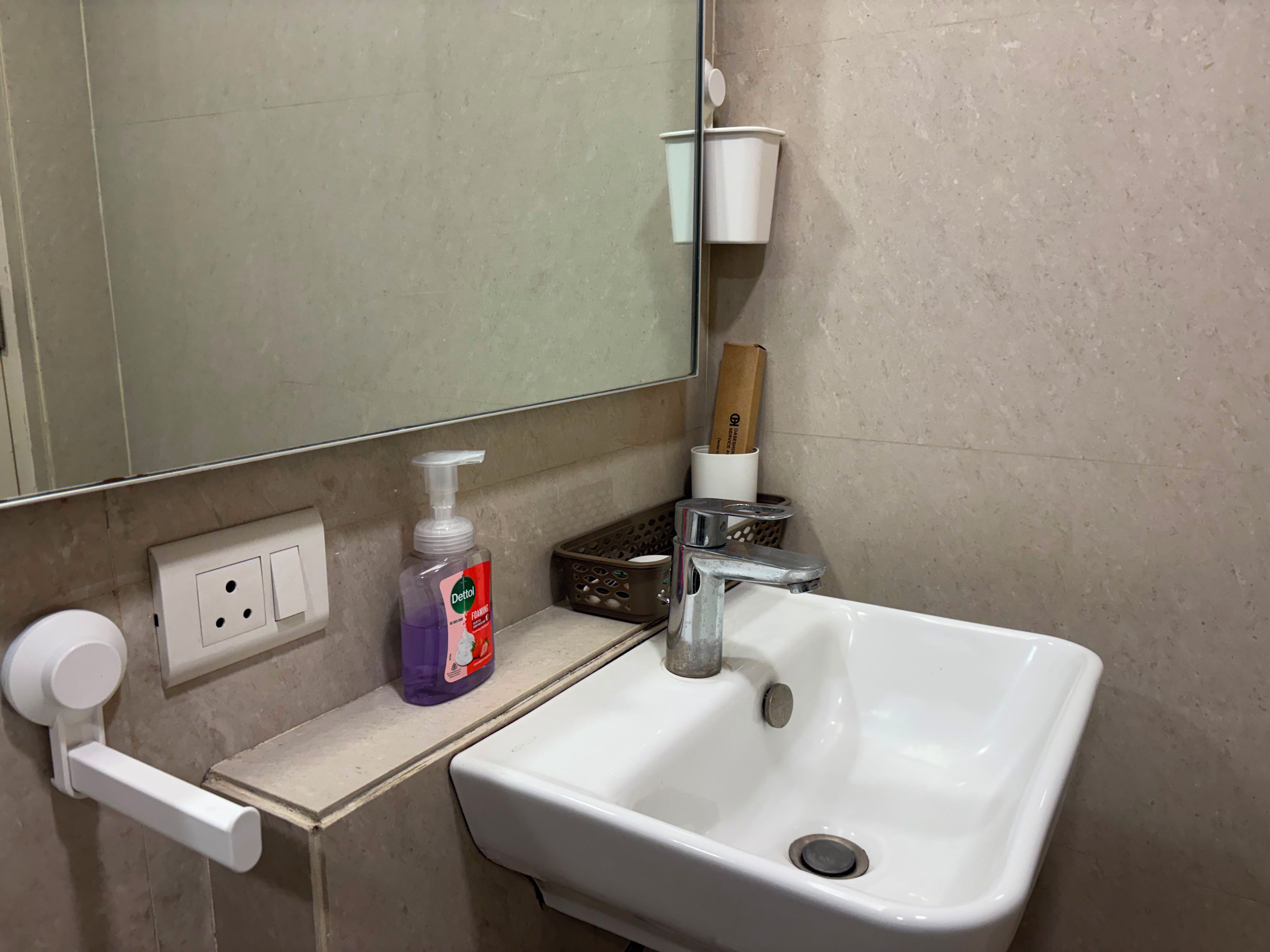 Une salle de bain avec un lavabo blanc, un miroir, un distributeur de savon et une bouteille de savon liquide Dettol pour les mains.