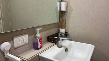 Ett badrum med ett vitt handfat, en spegel, en tvåldispenser och en flaska med Dettol-handtvål.