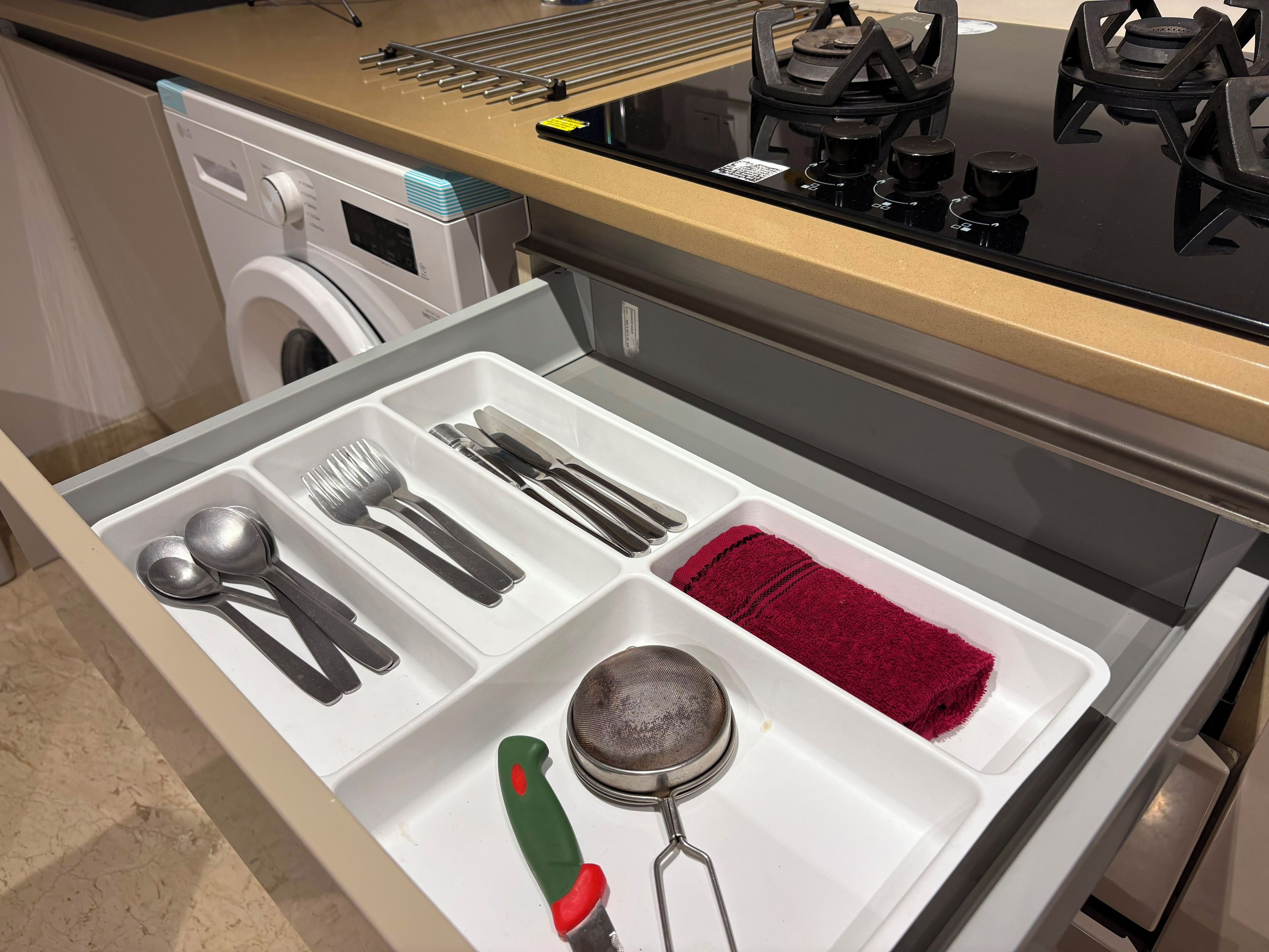 Un cajón de cocina con utensilios, un colador y una toalla roja.