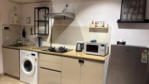 Cozinha compacta com máquina de lavar, micro-ondas e chaleira.