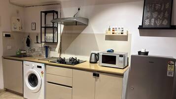 A compact kitchen with a washing machine, a microwave, and a kettle.