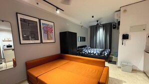 Quarto moderno com sofá-cama, escrivaninha, cadeira, guarda-roupa, cama com colcha estampada, espelho e telefone.