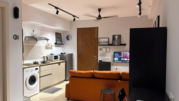 Um espaço compacto com cozinha compacta, sofá, televisão e ventoinha de teto.