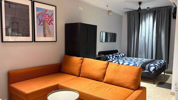 A modern hotel room with a sofa, a small round table, a bed with patterned bedding, a wardrobe, and two framed pictures on the wall.