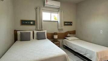 Quarto de hotel com duas camas, janela com cortinas, aparelho de ar condicionado e piso em azulejos.