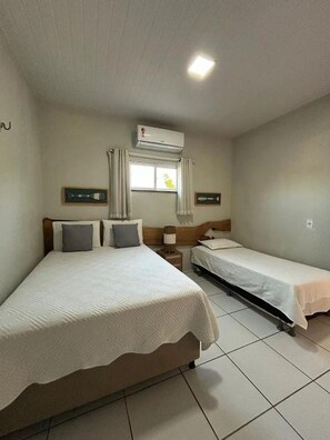 A hotel room with two beds, a window with curtains, an air conditioning unit, and a tiled floor. - Vagner's house (Grajaú)