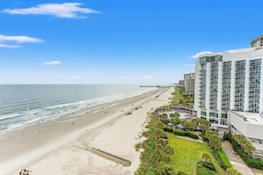 Een strandhotel met een zandstrand, uitzicht op de oceaan en een parkeerplaats met parasols.