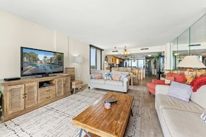 A spacious living room with a television, sofas, a coffee table, and a kitchen in the background. - Arcadian II 10F 3BR Condo in Shore Drive (Myrtle Beach)