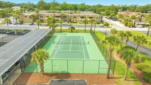 A tennis court with a surrounding fence, adjacent parking, and a building with multiple windows in the background. - Arcadian II 10F 3BR Condo in Shore Drive (Myrtle Beach)