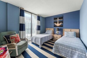 Een hotelkamer met twee bedden, een stoel, een nachtkastje en een raam met gordijnen.