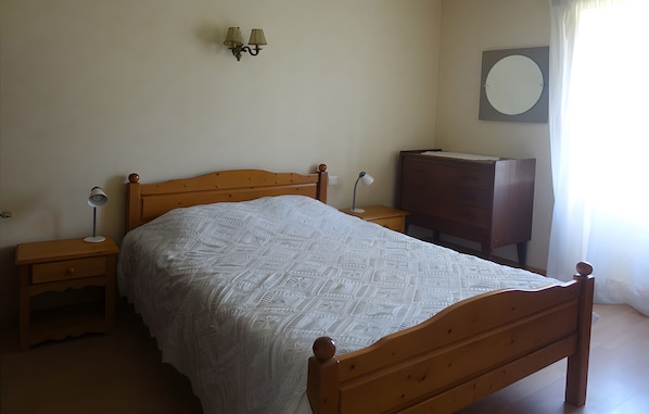 A bedroom with a wooden bed, a nightstand, a dresser, and a wall-mounted lamp.