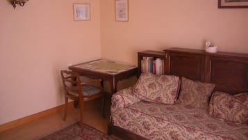 A room with a wooden table, a chair, a sofa, a bookshelf, and two framed pictures on the wall.