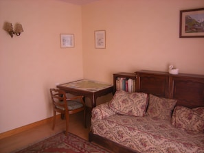A room with a wooden table, a chair, a sofa, a bookshelf, and two framed pictures on the wall.