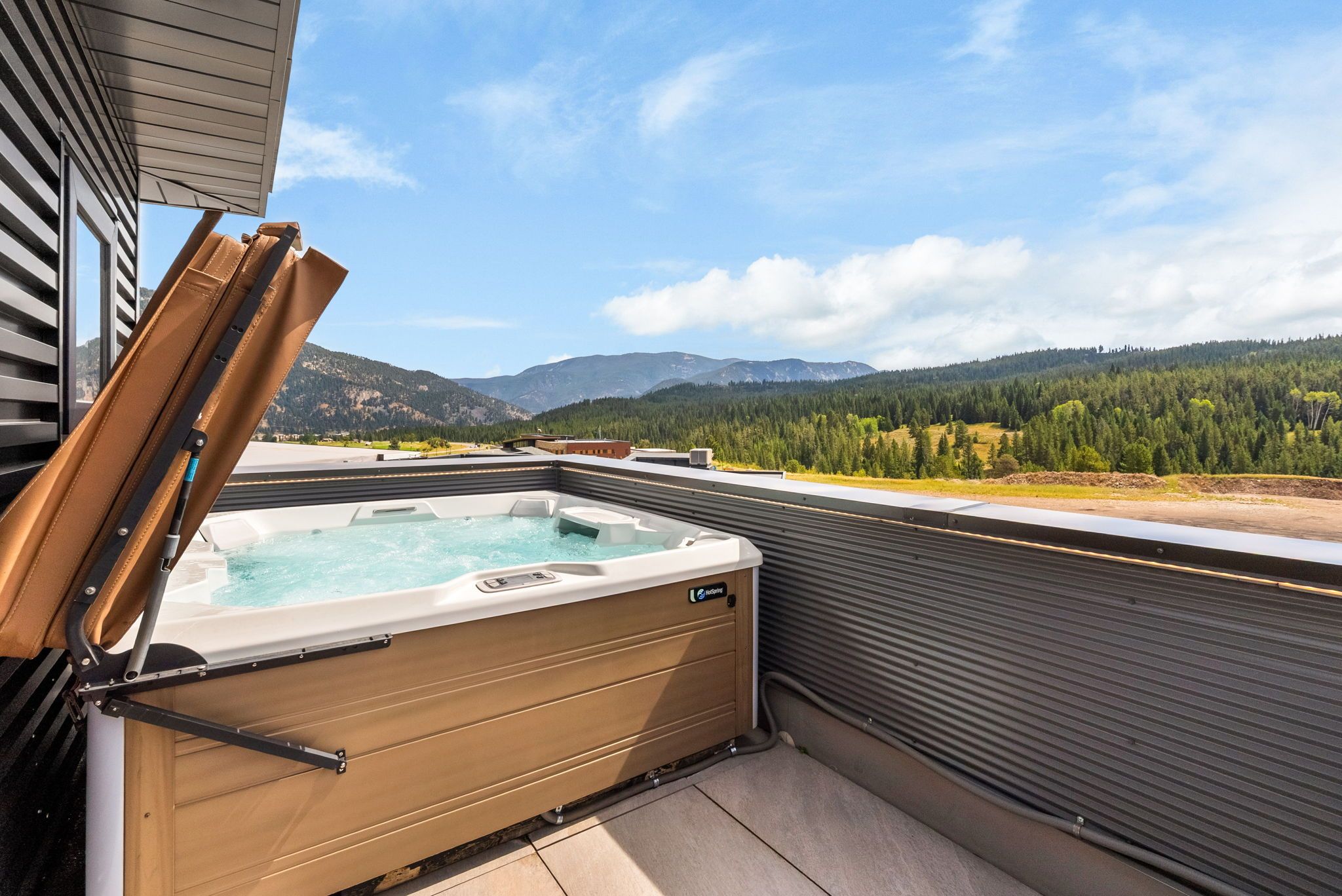 Un jacuzzi en una terraza exterior con vistas a montañas y bosque.
