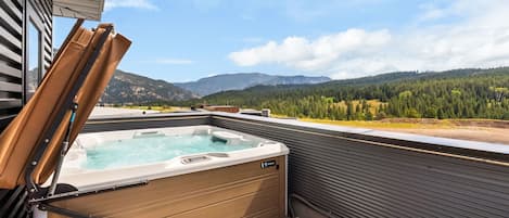 Un jacuzzi en una terraza exterior con vistas a montañas y bosque.