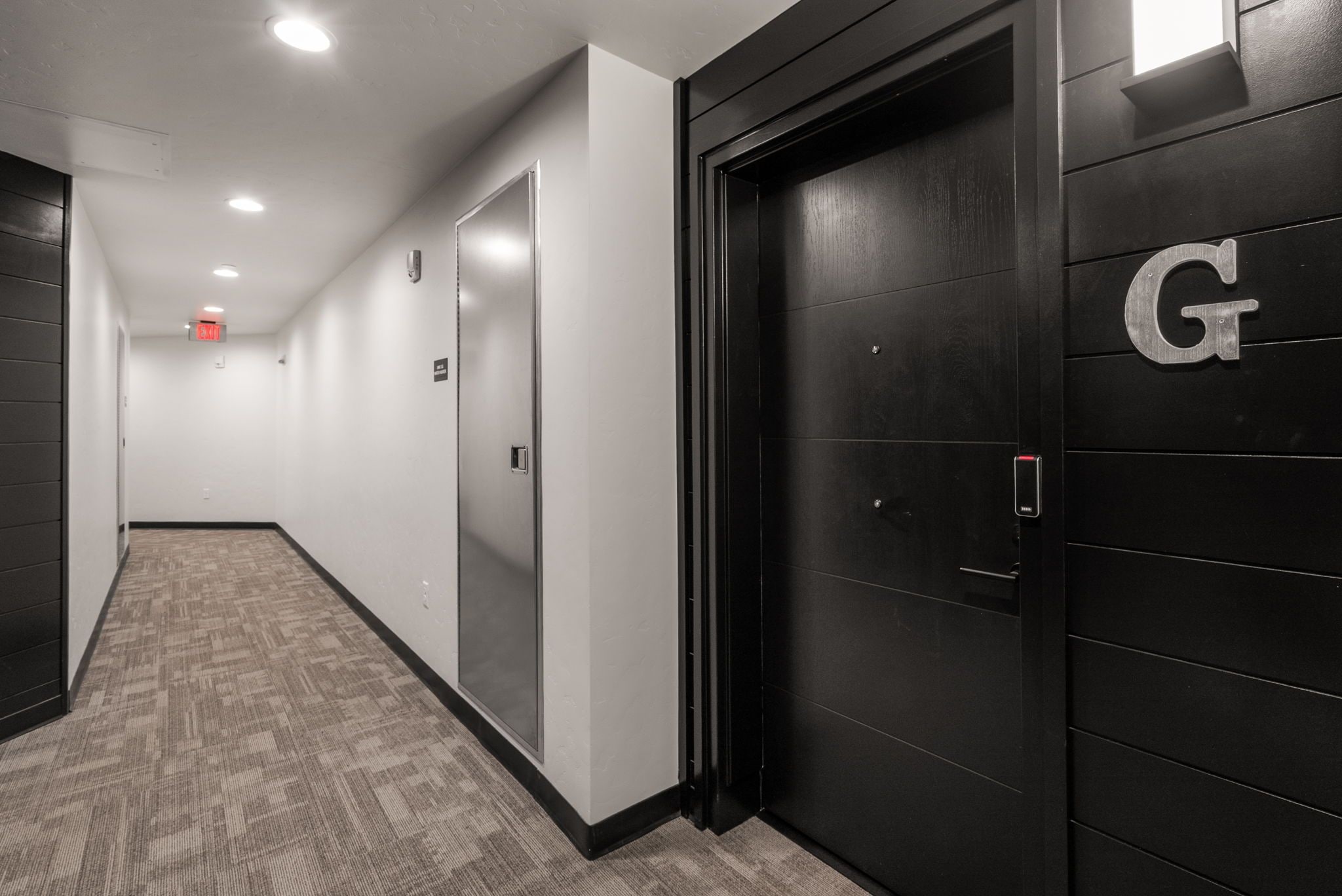 A hallway with a carpeted floor, a door with a 'G' sign, and a fire alarm on the ceiling.