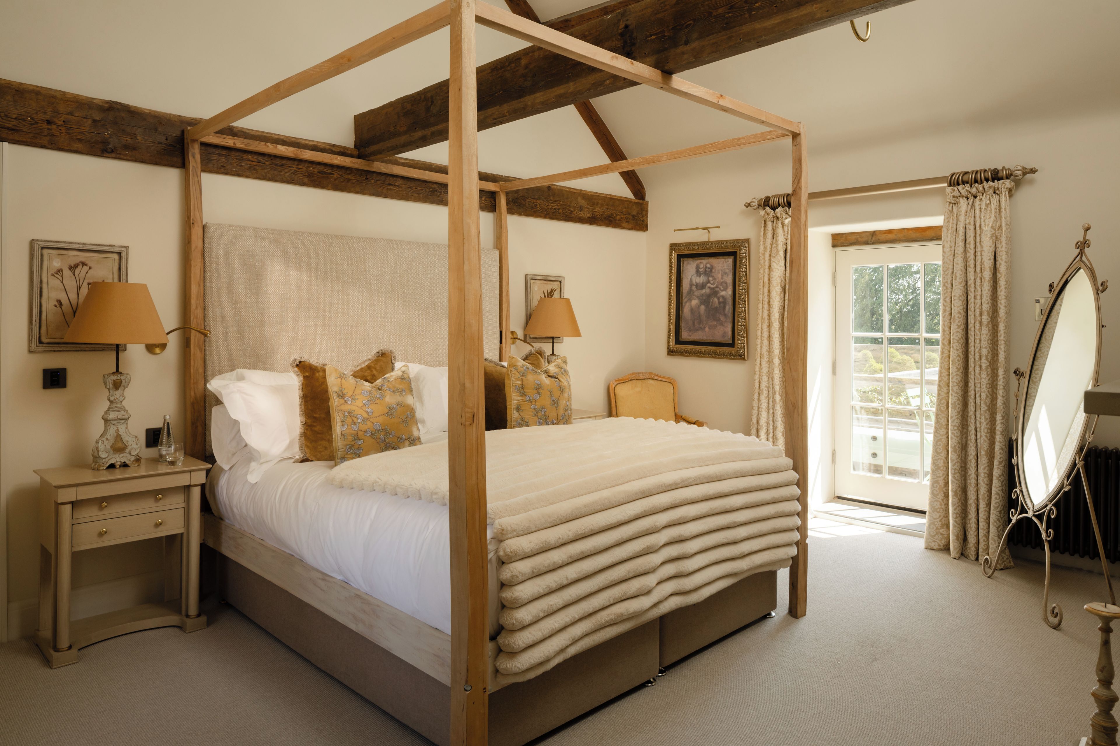 A four-poster bed with a wooden frame, two bedside tables with lamps, a large mirror, and a window with curtains.